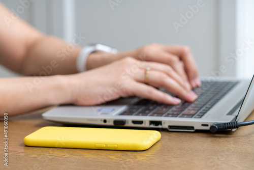 Women typing on laptop with yellow smart phone on wooden table