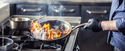 Foto Chef in the kitchen leans pan to the side for alcohol in it to catch fire for ga