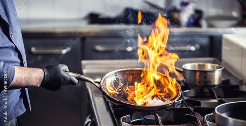 Chef holding pan performing flambe on a dish in it photo