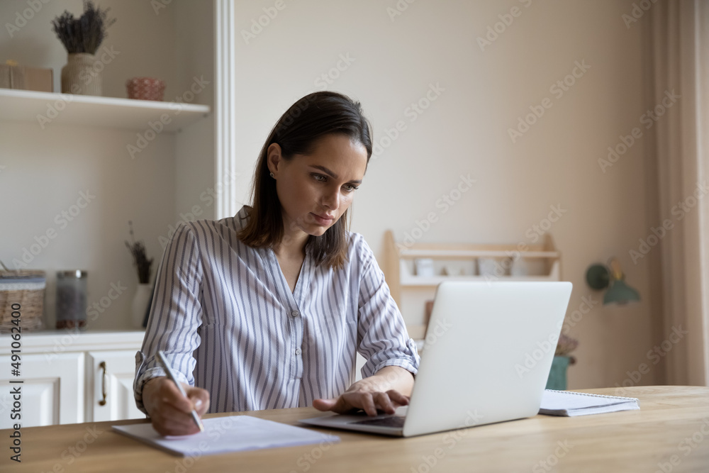 Business woman sit at table holds pen make correction in document, check written data, do paperwork looks at laptop, work from home in quarantine, student prepare essay, learn at home use tech concept Business woman sit at table holds pen make correction in document, check written data, do paperwork looks at laptop, work from home in quarantine, student prepare essay, learn at home use tech concept