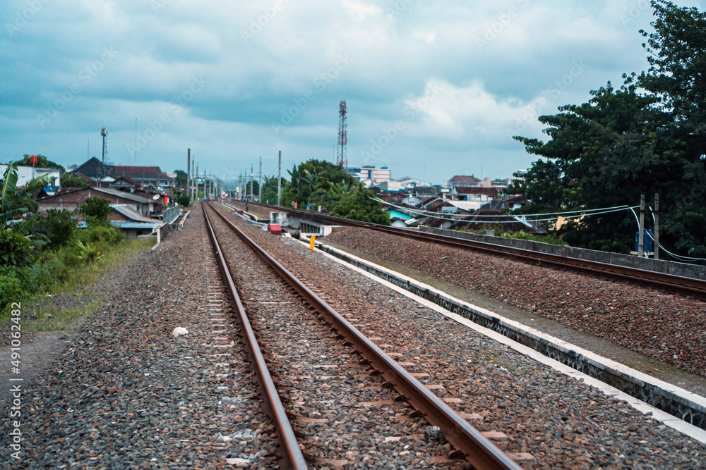  A railroad track made of iron, wood and gravel in a suburban area on a cloudy day in Indonesia