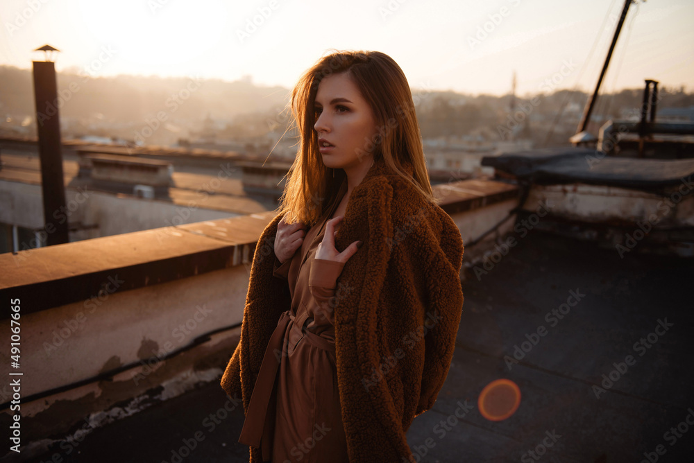 Young woman in dress posing on rooftop at sunset