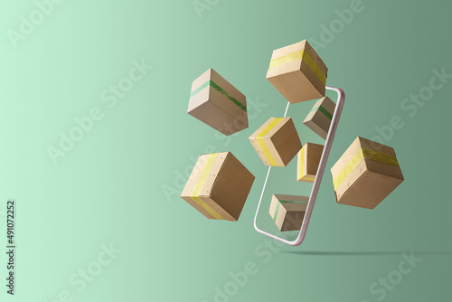 Concept of online delivery or shopping. Cell phone with flying out cardboard boxes on a green background.