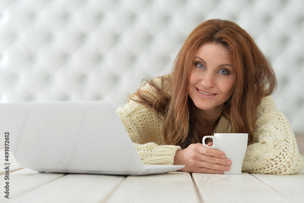 Beautiful young woman with laptop sitting on floor and drinking coffee Beautiful young woman with laptop sitting on floor and drinking coffee