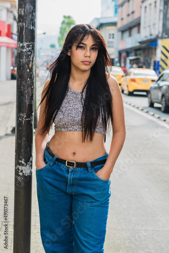 beautiful latina girl with brown skin posing very serious for the camera and focused on the photo shoot. university student waiting for transportation. fashion and beauty concept outside.