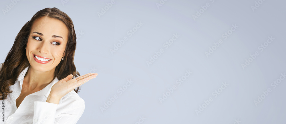Happy smiling woman in white confident blouse giving, holding or showing something or copy space for some text or imaginary. Business concept. Gray background. Brunette businesswoman. Wide image Happy smiling woman in white confident blouse giving, holding or showing something or copy space for some text or imaginary. Business concept. Gray background. Brunette businesswoman. Wide image