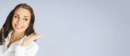 Happy smiling woman in white confident blouse giving, holding or showing something or copy space for some text or imaginary. Business concept. Gray background. Brunette businesswoman. Wide image