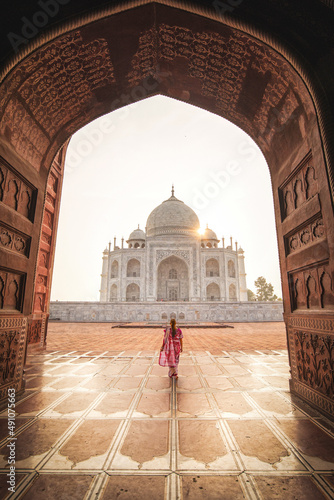 Woman wearing a red sari looking at the Taj Mahal at sunrise