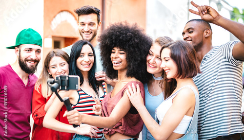 Multiracial friends taking selfie with mobile smart phone on stabilizer gimbal - Life style concept with milenial people having fun together sharing live feeds on social media channels - Bright filter photo