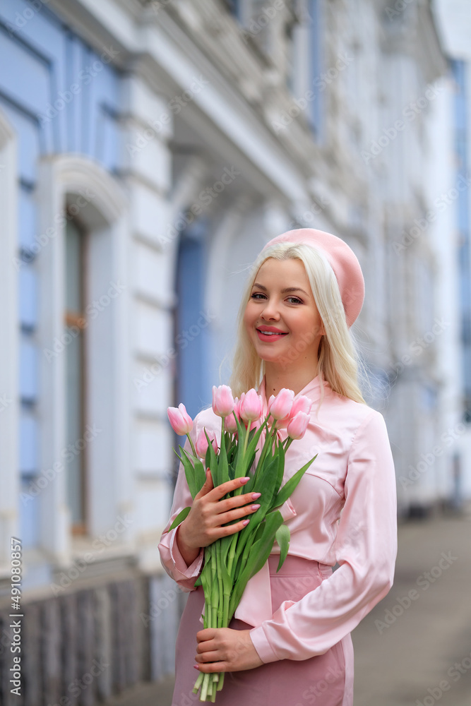 Fototapeta premium Girl holds bouquet of flowers and inhales their fragrance. Pretty girl takes lovely tulips with joy and smile. Portrait of surprised woman smelling flowers on the street.Girl holds bouquet of flowers
