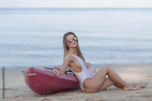 Beautiful slender young girl in a white swimsuit near the kayak