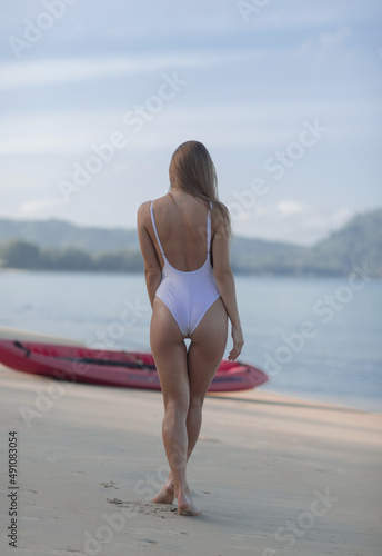 Beautiful slender young girl in a white swimsuit near the kayak © fotoplaton