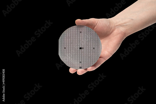 A hand holds a multilayer semiconductor silicon wafer with a microcircuit chip of a powerful Darlington transistor isolated on a black background photo