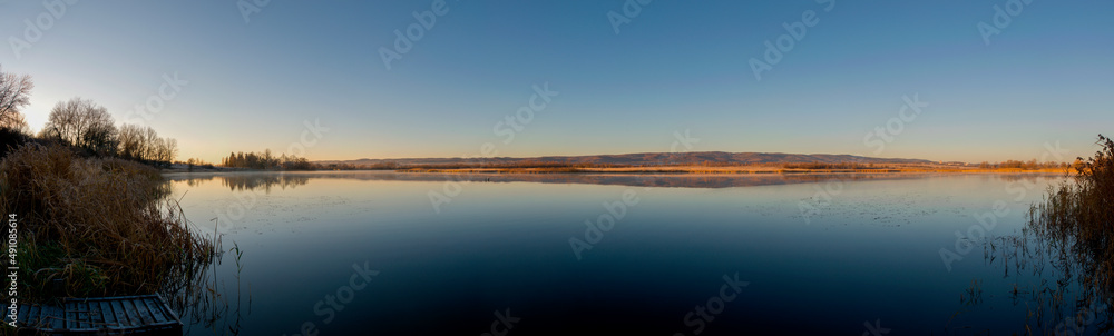 Panorama of autumn lake. Mirror reflection in water, blue sky.