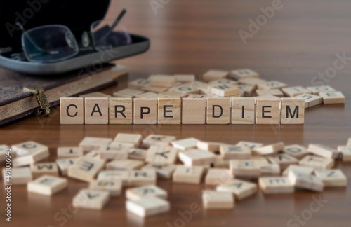 carpe diem word or concept represented by wooden letter tiles on a wooden table with glasses and a book photo