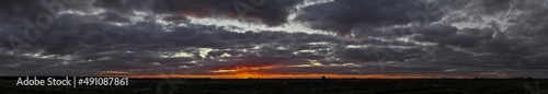 Wide panorama of a flat landscape with dark clouds at sunset