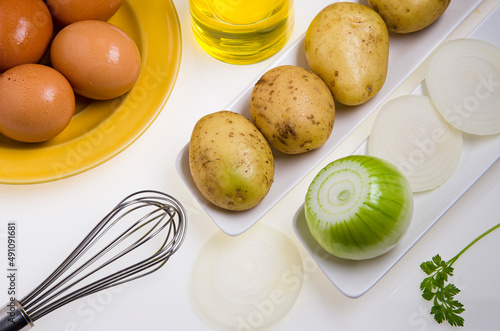 Ingredients on a table for the preparation of a potato omelette, based on potatoes, onion and eggs.