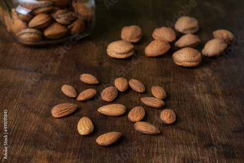 Almonds on a dark wooden table, next to some seeds.