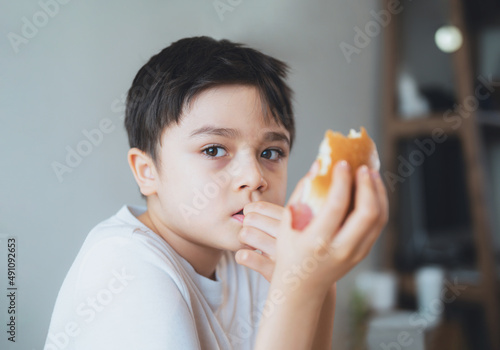 Hungry young boy eating homemade bacon sandwiches with mixed vegetables  Healthy Kid having breakfast at home  Child bitting finger nails and looking out with thinking face