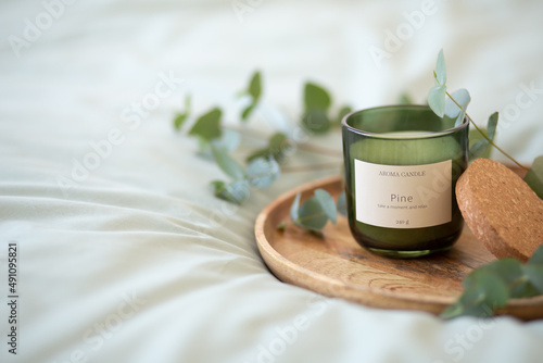 Green scented candle and a branch of eucalyptus on a wooden tray.