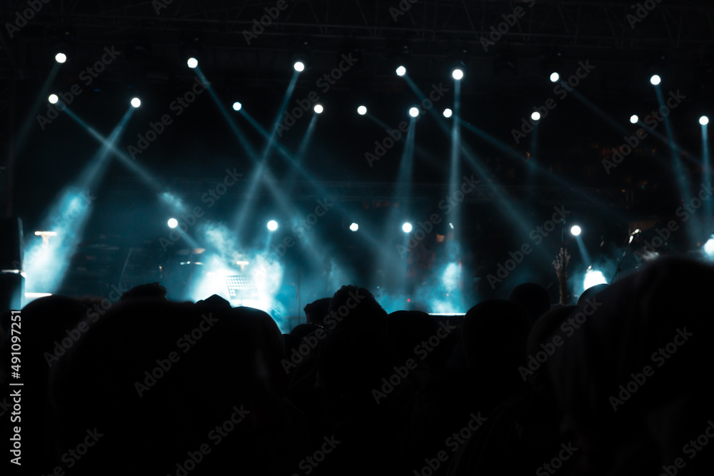 Silhouette of people in a concert hall. Spotlights on the stage.