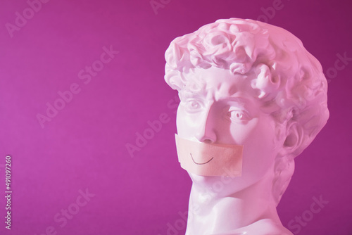 copy of the head of an antique statue of David with a taped mouth in pink neon light on a purple background photo