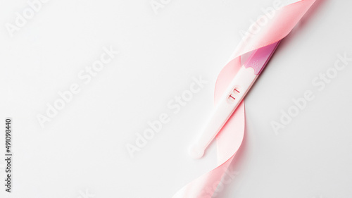 Positive pregnancy test result. Woman pregnant test with pink silk ribbon on white background. Medical healthcare gynecological, pregnancy fertility maternity people concept. photo