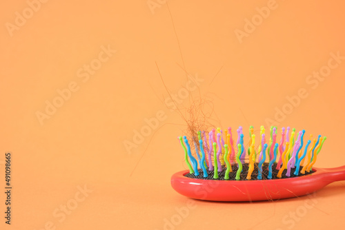 hair and red plastic massage comb on orange background