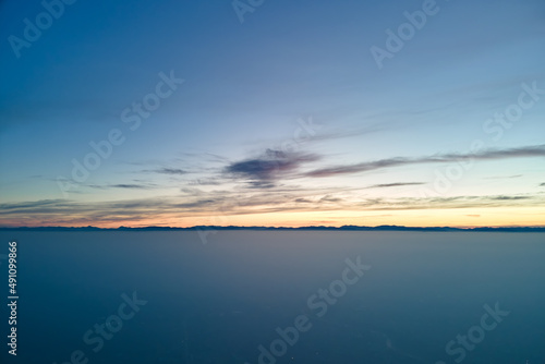 Aerial view of colorful sunset over white dense foggy clouds cover with distant dark silhouettes of mountain hills on horizon