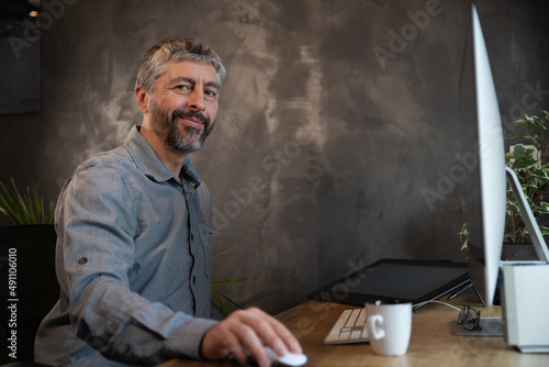 portrait d'un homme de 50 ans qui travaille devant un ordinateur dans son bureau. Il travaille à distance à la maison en télétravail. Il est zen et détendu.