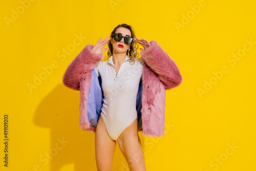 Gorgeous young woman posing in luxurious fur coat and bodysuit. Fashion, beauty. Studio shot.