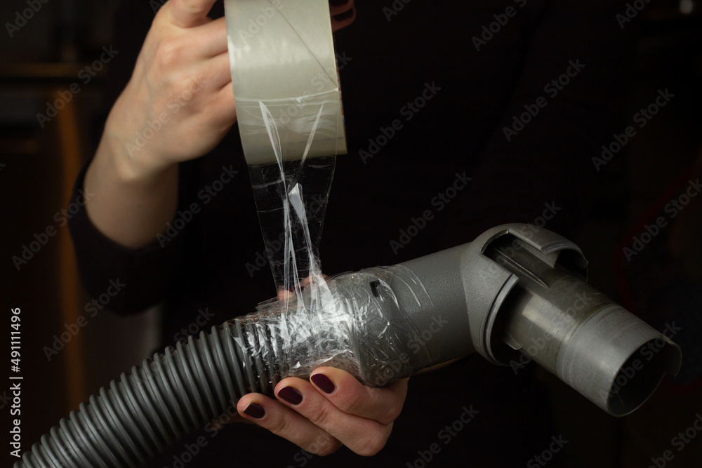 A woman is fixing a broken vacuum cleaner hose with a duct tape.