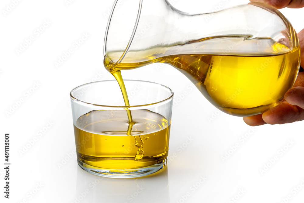 Extra virgin olive oil being poured from decanter into glass cup on white  background Photos | Adobe Stock