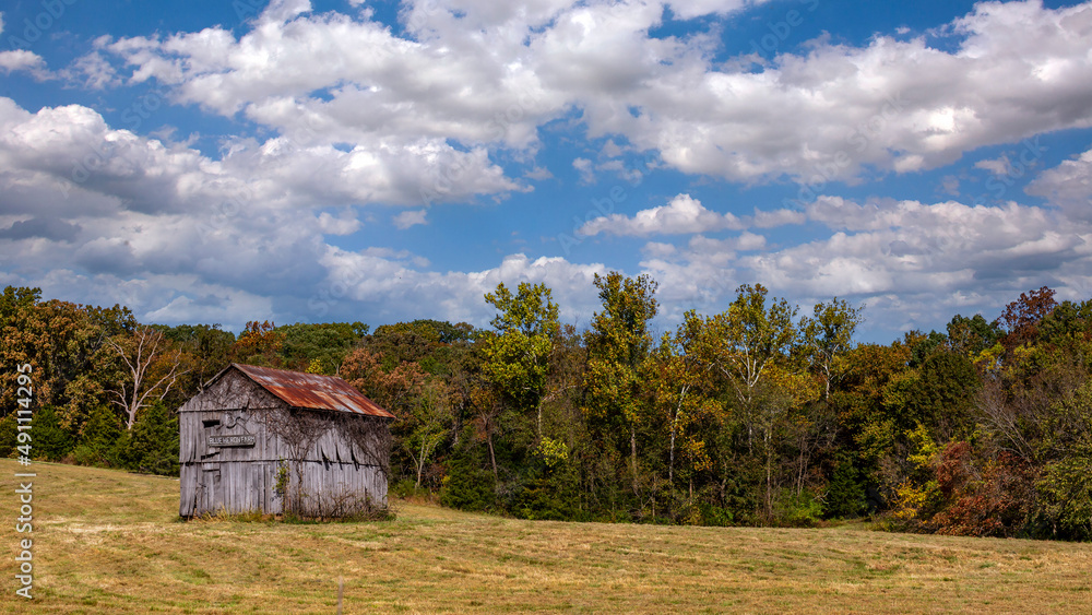 Fototapeta premium Old weatherworn barn in a rural countryside field under a cloudy sky in Missouri