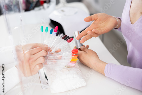 Professional manicurist helping woman client to choose color of nail polish, cropped shot of female hands holding palette..