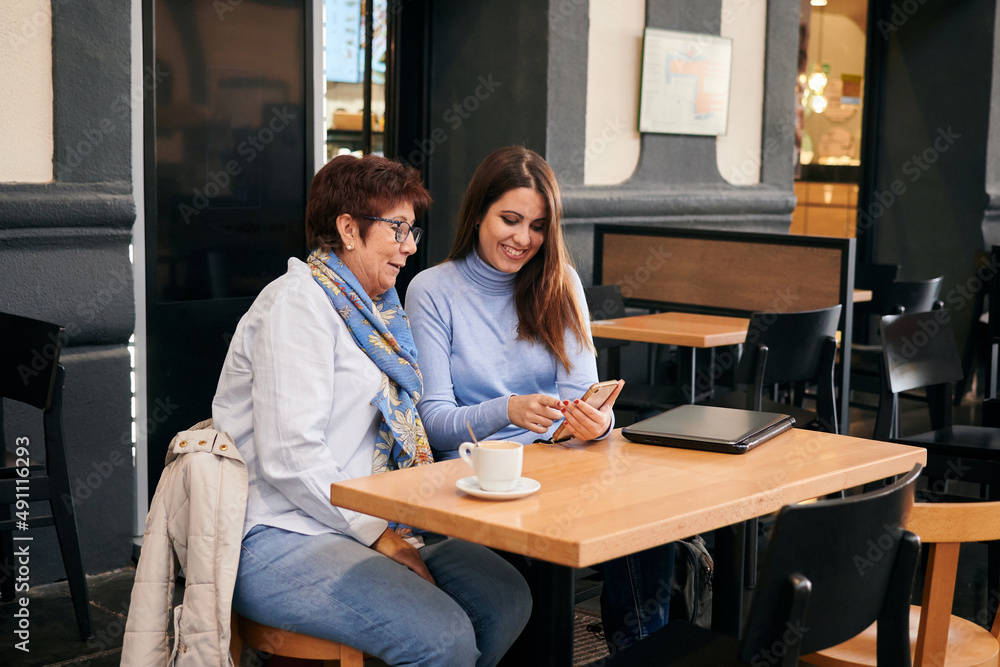 Mature woman and young woman look at a mobile phone in a coffee shop Mature woman and young woman look at a mobile phone in a coffee shop
