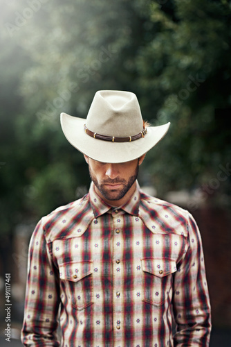 Kings have crowns, but a cowboy only has one hat. Shot of a handsome cowboy wearing a check shirt and stetson. © Mariusz S/peopleimages.com