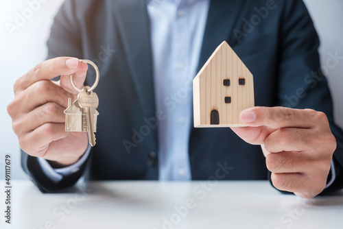 Businessman hand holding key with wooden Home model. Real estate, buy and sale, Property insurance, rental and contract agreement concepts