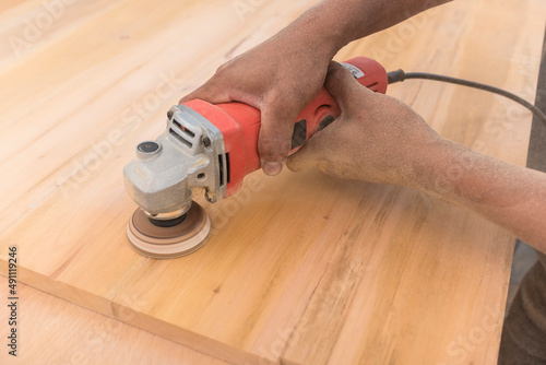 Using an angle grinder with a sanding disc attachment to level the surface of a sheet of plywood to be used for furniture or cabinetry.