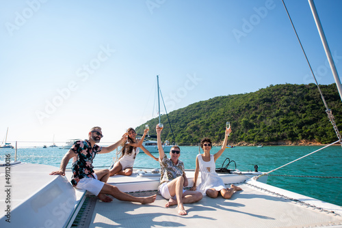 Group of Caucasian people friends enjoy luxury party drinking champagne together while catamaran boat sailing in the ocean. Man and woman relax outdoor lifestyle sail yacht on tropical travel vacation