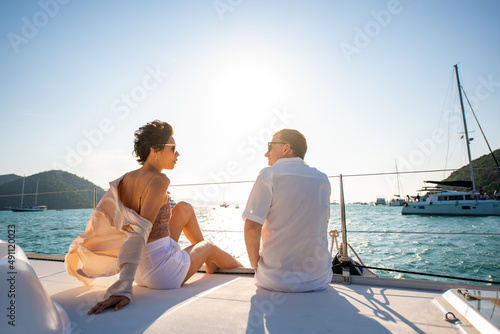 Caucasian couple enjoy outdoor luxury party drinking champagne with talking together while catamaran boat sailing at sunset. Man and woman relax with outdoor lifestyle on summer travel vacation © CandyRetriever 