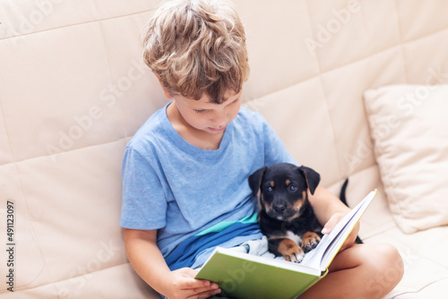 A boy with a little dog is reading a book