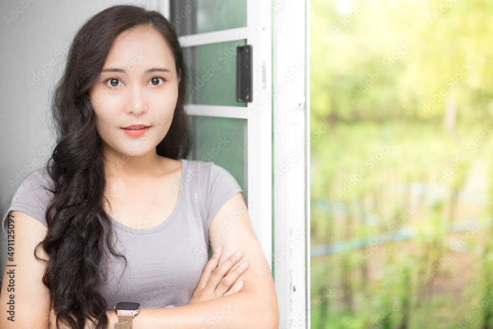 Beautiful Asian business woman wearing grey casual shirt relaxing at the window and admiring nature and copy space.  Confident Asian working woman smiling and cheerful