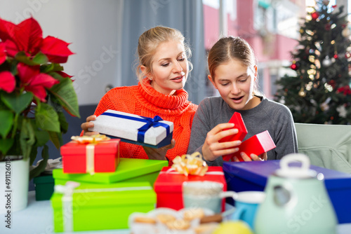 Smiling woman and her teenage daughter opens Christmas gift boxes with presents near the New Year tree © JackF