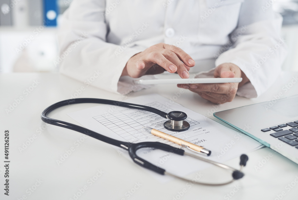 Digital tablets are recommended by doctors. Cropped shot of an unrecognizable female doctor using a digital tablet while working in her office. Digital tablets are recommended by doctors. Cropped shot of an unrecognizable female doctor using a digital tablet while working in her office.
