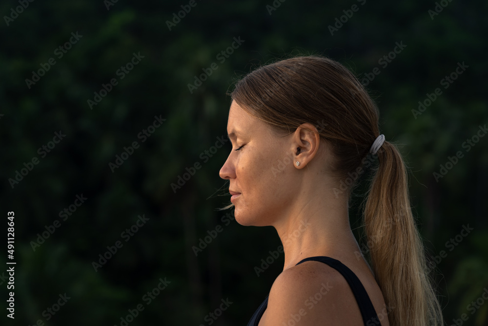 Portrait of a young woman meditating at sunrise with her eyes closed. Forest in the background . Portrait of a young woman meditating at sunrise with her eyes closed. Forest in the background .