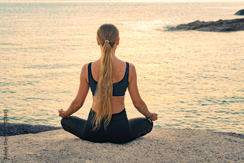 Young caucasian woman with long hair meditating in a black clothes for yoga on a rocks on the top by the sea.