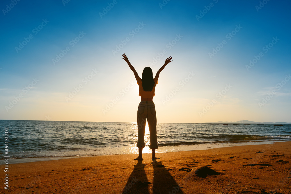 silhouette happy young woman enjoying freedom with open hands on sea at sunset