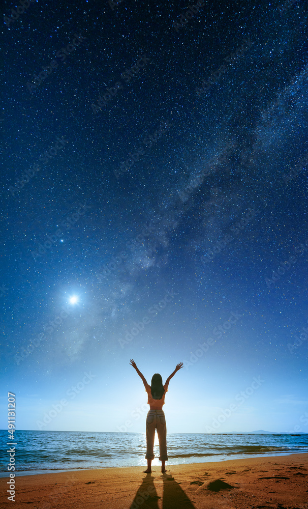 Silhouette of happy woman standing on the beach under starry night sky with milky way