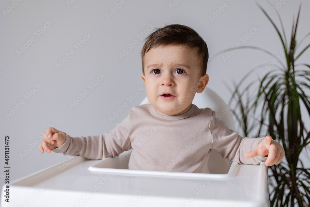 cheerful smiling baby is sitting in a white high chair for feeding. white background cheerful smiling baby is sitting in a white high chair for feeding. white background